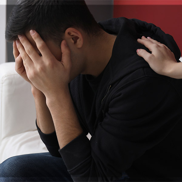 Distressed man puts hands over his face. A woman's hand is on his shoulder.