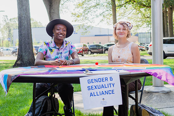 Two students outside tabling for their organization, Gender and Sexuality Alliance.