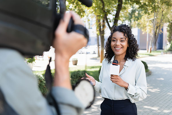 Cameraman with video camera near smiling african american reporter with microphone