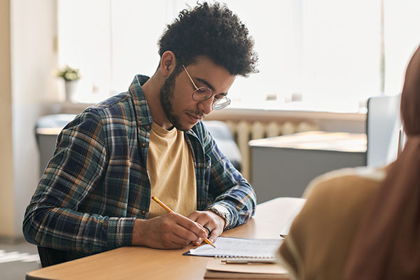 Student sitting at table and writing exam with other students in class