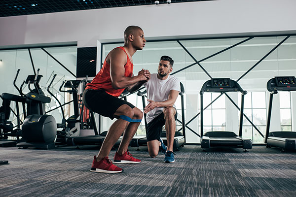 Attentive trainer working out with young African American exerciser warming up in a gym